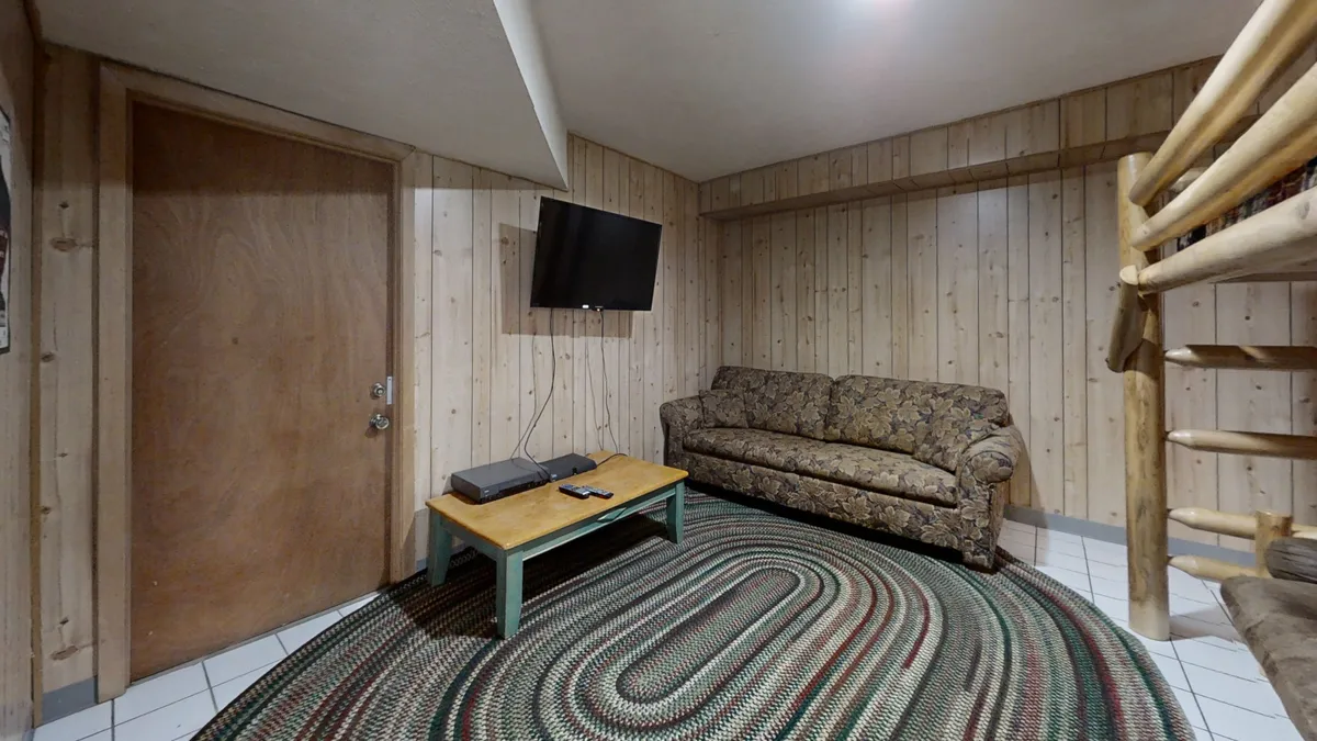 A comfortable living space with a sofa, TV, coffee table, wooden walls, and a bunk bed. The area is designed for relaxation, movie nights, or playing games, making it ideal for families to unwind together after exploring local attractions.