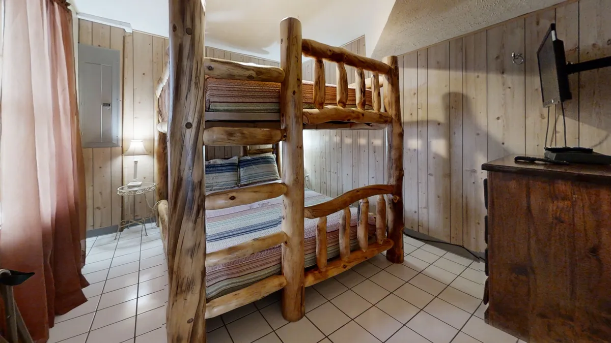 This image showcases a bunk bed surrounded by wooden furniture and textured walls, creating an inviting and playful atmosphere. The space is suited for sleeping, reading, and playing games, catering to younger guests or groups needing flexible sleeping arrangements.