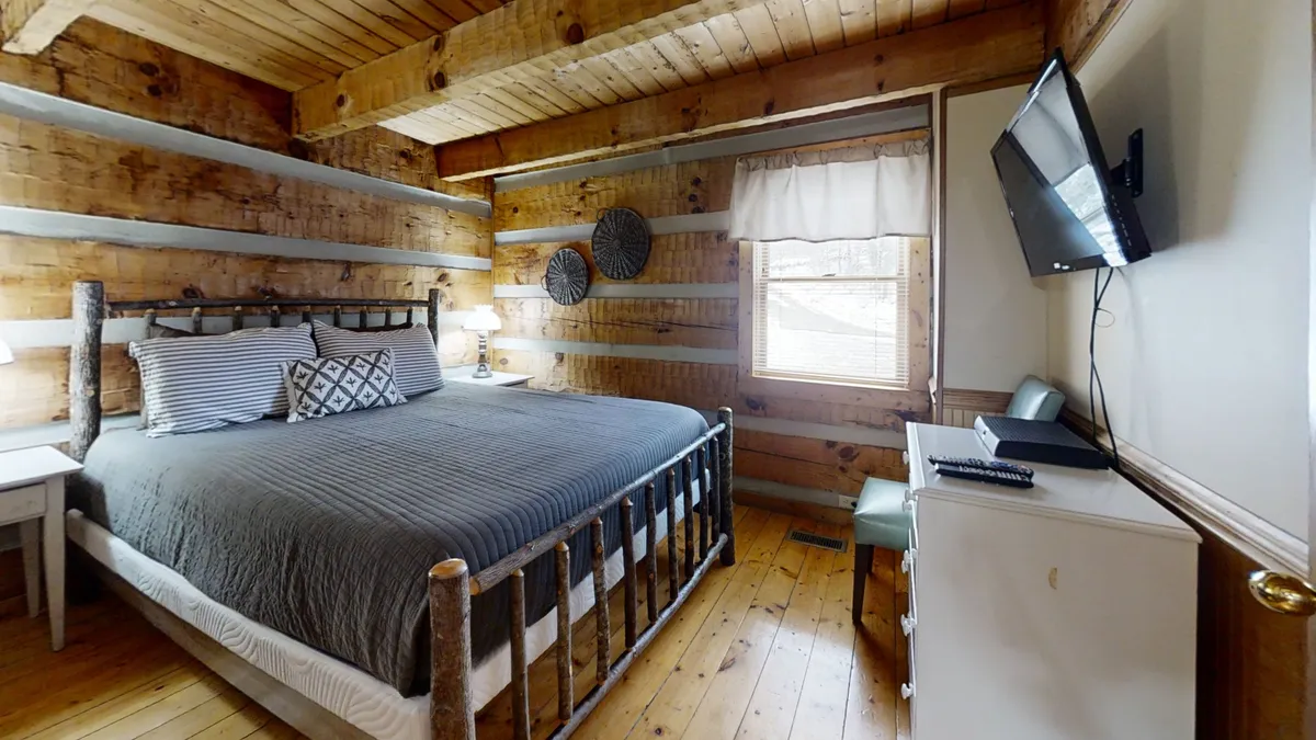 Displaying a rustic bedroom with a comfortable bed, wooden walls, decorative wall hangings, and a flat-screen TV, this scene radiates warmth and relaxation, perfect for unwinding after a day's adventures.