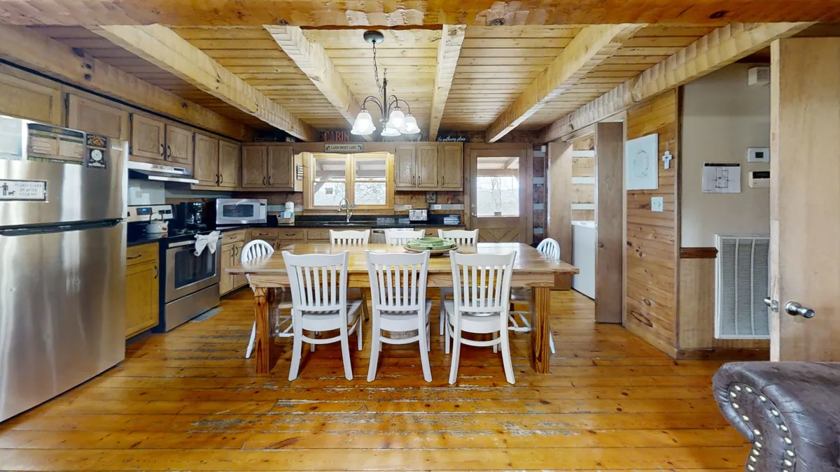 A large wooden dining table surrounded by white chairs takes center stage, adjacent to a fully equipped, modern kitchen with sleek appliances. The setting exudes a sense of warmth and togetherness, inviting shared meals and group activities.